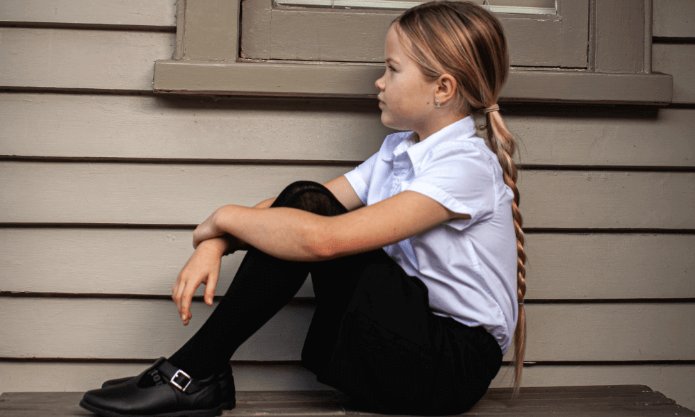 Child wearing premium navy wool tights and a school uniform, sitting on a bench with a thoughtful expression.