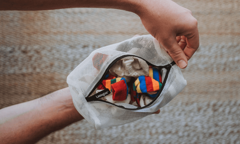 A person holding a mesh bag filled with colorful socks, demonstrating how to care for merino wool socks.