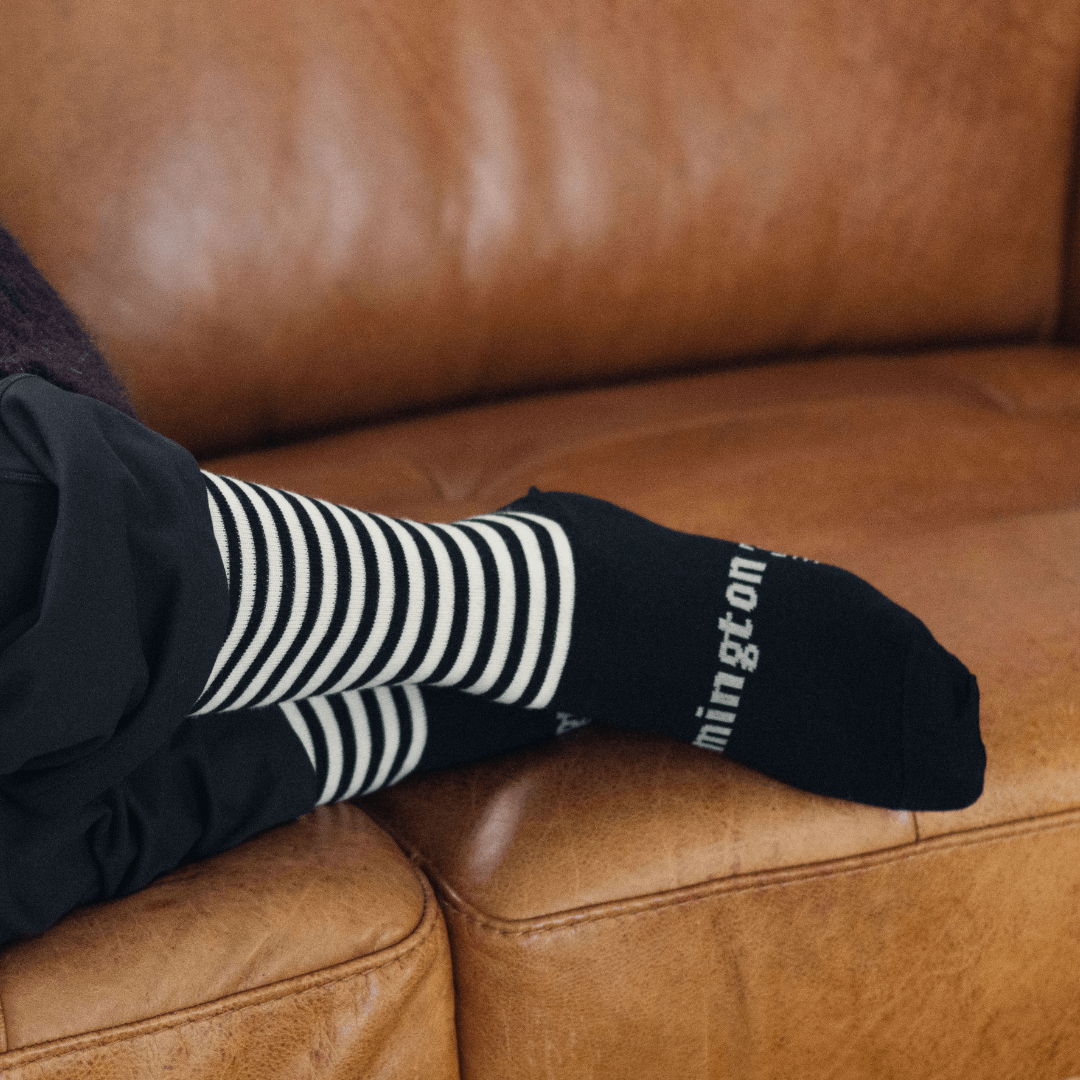 Merino Wool Crew Socks featuring black and latte stripes worn on a foot resting on a brown couch.